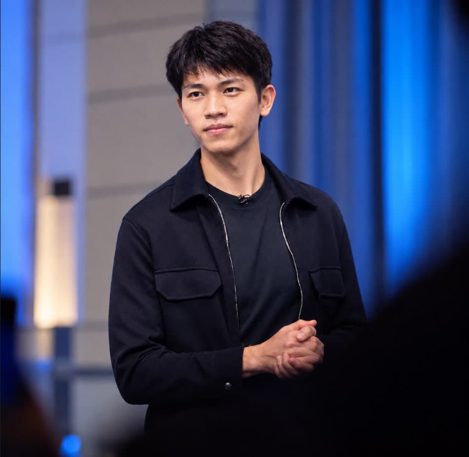 Chris Lim in a black jacket, standing before a blue-lit stage.